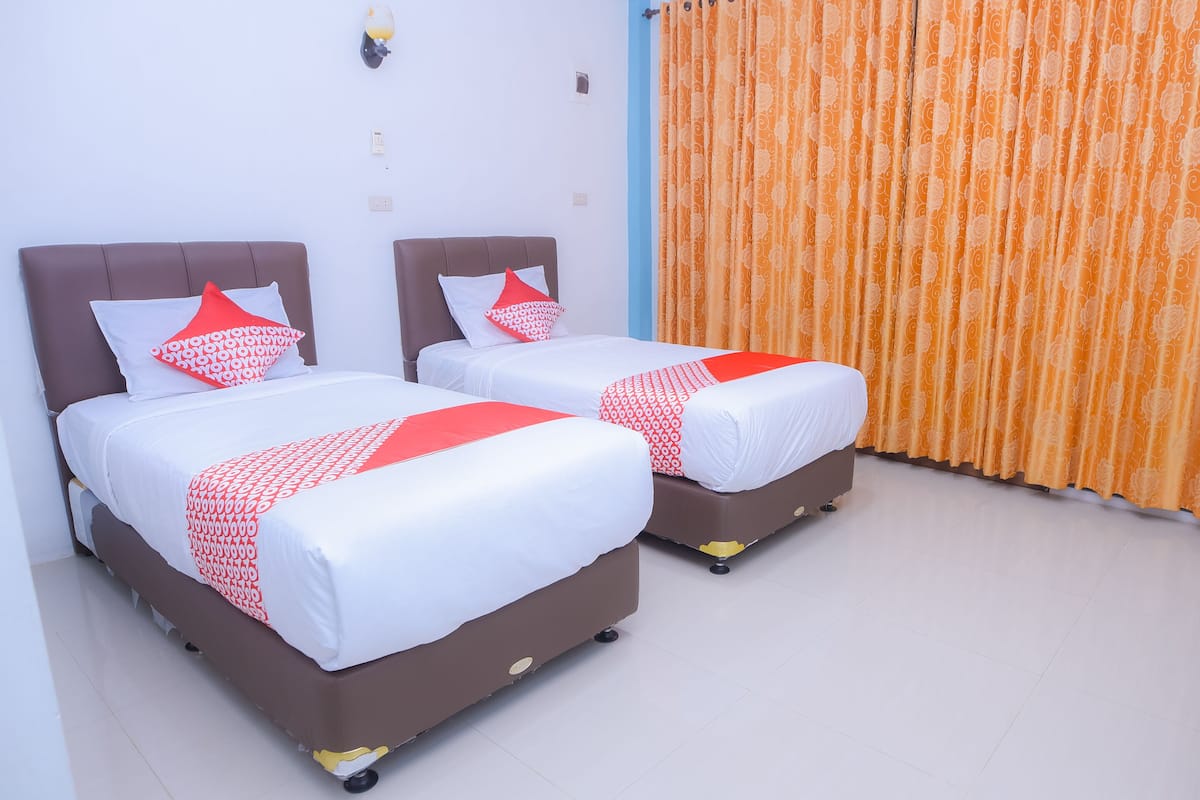 Two beds with brown headboards and white bedding, a red and white patterned throw, and an orange curtain.