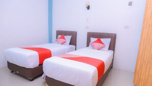 Deux lits simples avec une literie blanche et rouge, un mur d’accent bleu et un plafond blanc uni.