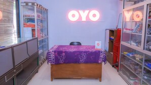 Une pièce avec une table violette, un lit et un panneau lumineux au néon sur lequel on peut lire « OYO ».