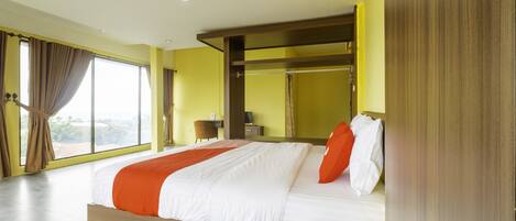 A modern hotel room with a large bed, a wooden headboard, and a view of the outdoors through large windows.