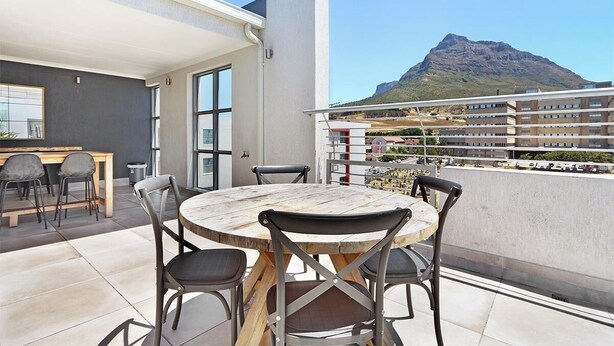 A balcony with a round wooden table and chairs, a small kitchen area, and a view of a mountain. - The Paragon 317 (Cape Town)