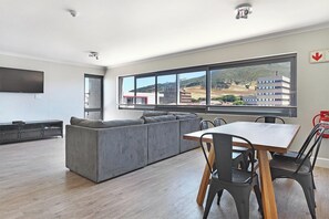 A modern living room with a grey sectional sofa, a wooden dining table with chairs, and large windows offering a view of buildings and hills. - The Paragon 317 (Cape Town)