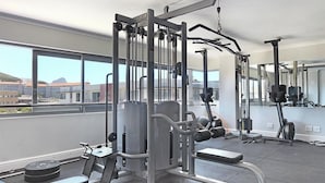 A gym with various exercise equipment, large windows, and a view of buildings and mountains. - The Paragon 317 (Cape Town)