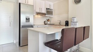 A modern kitchen with white cabinets, a stainless steel refrigerator, a microwave, and a coffee station. - The Paragon 317 (Cape Town)