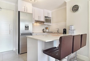 A modern kitchen with white cabinets, a stainless steel refrigerator, a microwave, and a coffee station.