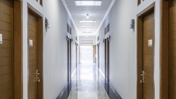 A hotel corridor with wooden doors, numbered room signs, and a shiny tiled floor.