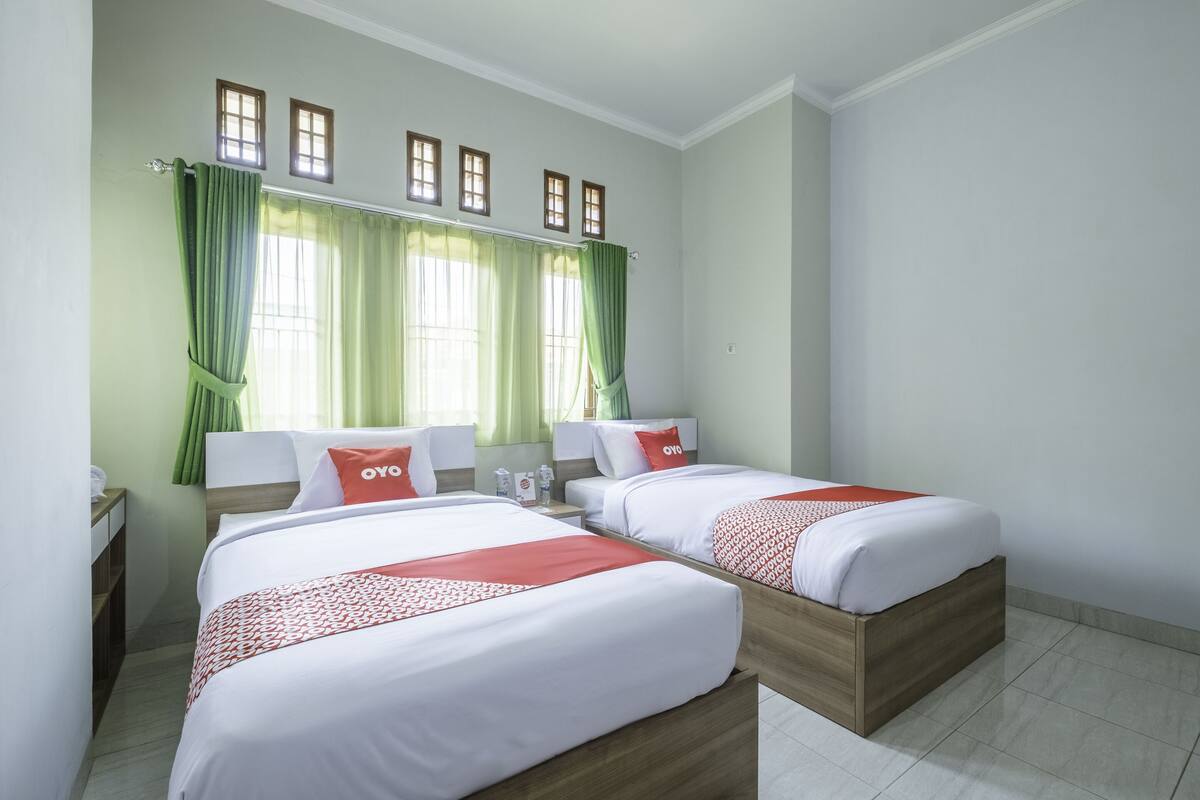 Een hotelkamer met twee bedden, groene gordijnen en een raam met houten kozijnen.
