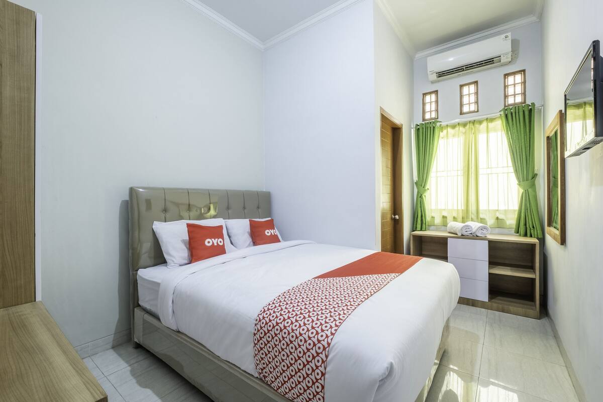 Een hotelkamer met een bed, een houten nachtkastje, een bureau met een stoel en een airconditioning.