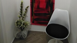 Un couloir orné d’un tableau abstrait rouge, d’une chaise blanche et d’une plante.