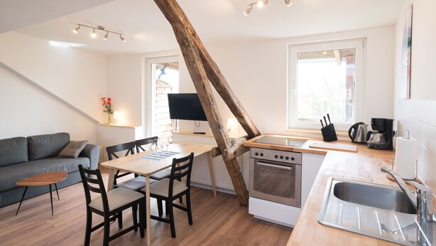 A modern kitchen with a wooden beam ceiling, a dining area with a table and chairs, and a built-in oven. - FeWo Engler Lüneburg Wallstraße (Lueneburg)