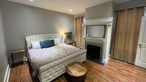 A bedroom with a large bed, a wooden side table, a fireplace, and a wardrobe. - Huge 5 bed, 5 bath in Historic Downtown Savannah (Savannah)