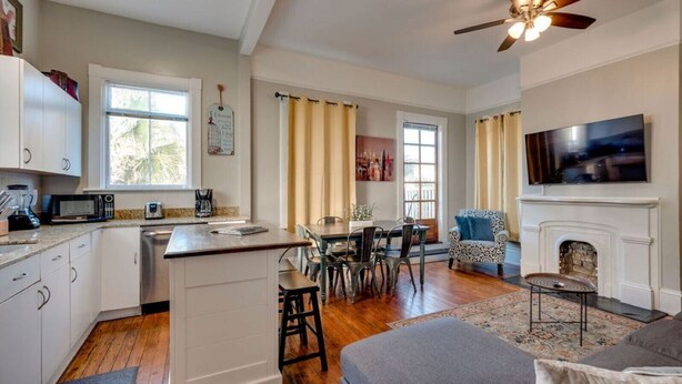 A spacious living area with a fireplace, a dining table, and a kitchen with white cabinets and a wooden floor. - Huge 5 bed, 5 bath in Historic Downtown Savannah (Savannah)