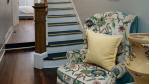 A staircase with wooden handrails and a floral-patterned armchair with a cushion. - Huge 5 bed, 5 bath in Historic Downtown Savannah (Savannah)