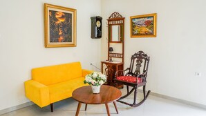 A room with a yellow sofa, a wooden rocking chair, a round wooden table with a vase of flowers, a wall clock, and two framed paintings. - OYO 1785 Villa Jeruk Ciwidey (Ciwidey)