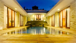 Ein modernes Gebäude mit Schwimmbad, Steinwänden und einem überdachten Bereich mit Treppen, die zu einer Terrasse führen.