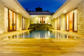 Ein modernes Gebäude mit Schwimmbad, Steinwänden und einem überdachten Bereich mit Treppen, die zu einer Terrasse führen.