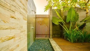 A modern bathroom with a stone wall, a wooden door, and a small pebbled area. - The Chandara Villa Bali (Nusa Dua)