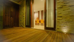 A wooden deck leading to a room with a stone wall and a sliding glass door. - The Chandara Villa Bali (Nusa Dua)