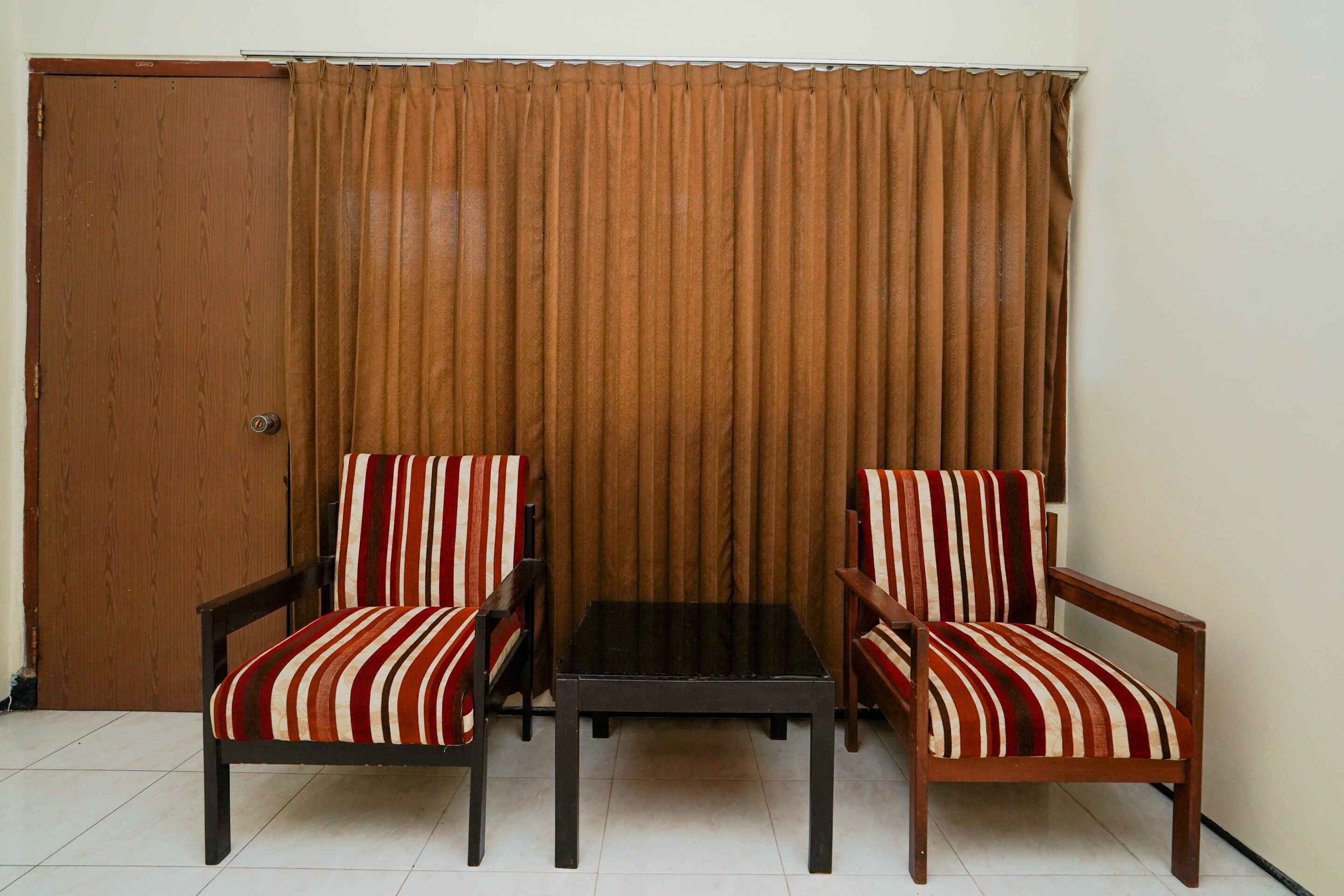 A room with two striped armchairs, a small table, and a brown curtain.