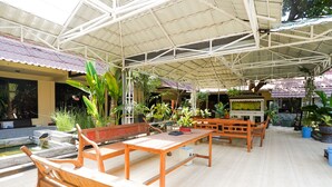 Een overdekt terras buiten met houten meubels en planten in potten.