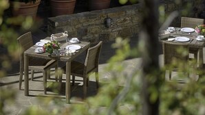 An outdoor dining area with wicker tables and chairs, stone walls, and potted plants. - Luxury Chianti in La Farfalla (Greve in Chianti)