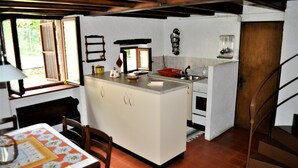 Una cocina compacta con una isla central, una mesa de comedor con sillas y una escalera que sube a un nivel superior.