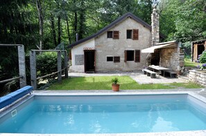 A stone house with a swimming pool, a stone fireplace, and a small garden.