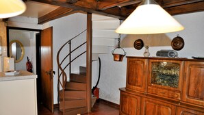 Una escalera de madera, una mesa de comedor con sillas, un aparador de madera con cristalería y una lámpara colgante.