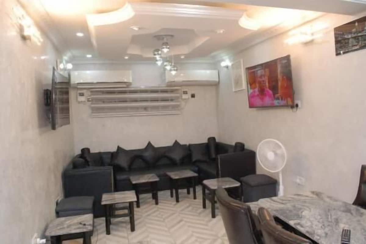 A modern living room with a sectional sofa, a coffee table, a fan, and a painting on the wall.