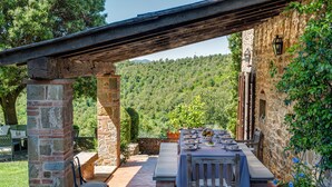 An outdoor dining area with stone pillars, a wooden pergola, and a view of a forested hillside. - Luxury Privacy in the Heart of Tuscany (Pienza)