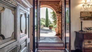 An arched doorway leading to a garden with a tall tree, a stone wall, and a wooden bench. - Luxury Privacy in the Heart of Tuscany (Pienza)