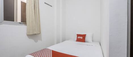 A small, single-bed room with white walls, a window with a curtain, and a bed with a red and white patterned blanket.