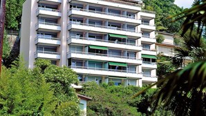 Un edificio de varios pisos con balcones, rodeado de abundante vegetación.