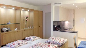 Un dormitorio con una cama, una mesita de noche pequeña y una mesilla auxiliar. Cuenta con una kitchenette con un lavamanos y una estufa.
