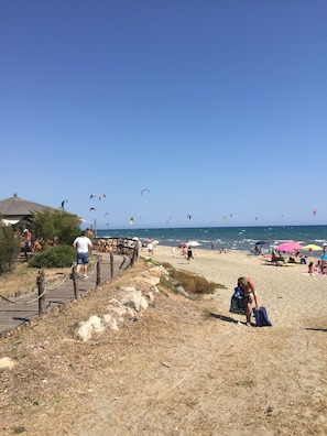 Ein Strand mit einer Holzpromenade, Sonnenschirmen und Menschen, die das Meer genießen.