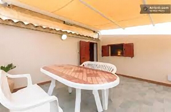 A covered outdoor area with a round table and two white plastic chairs.