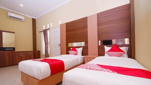 A hotel room with two beds, a wooden headboard, a mirror, a wardrobe, and a window with curtains.