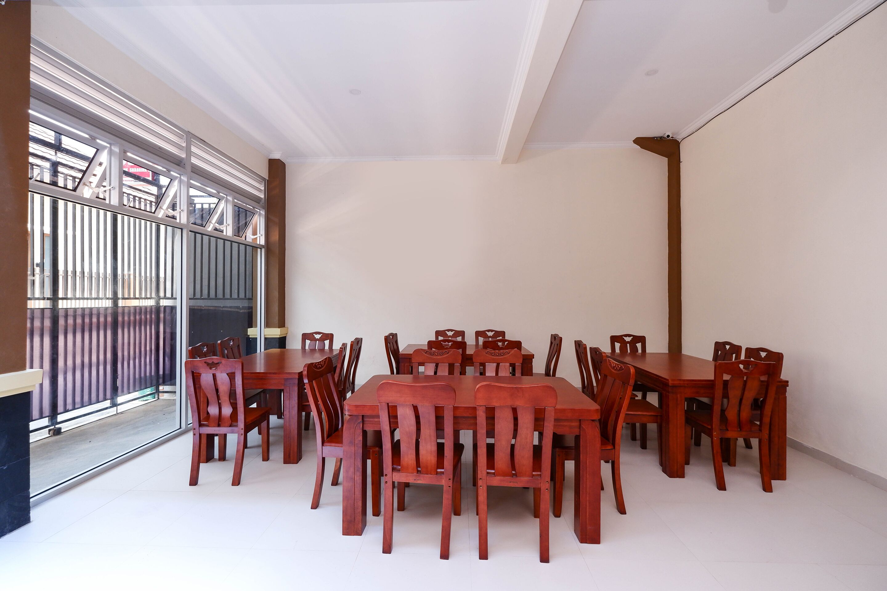 A dining area with a large wooden table and chairs, a glass door leading outside, and a white ceiling.
