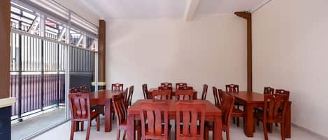 A dining area with a large wooden table and chairs, a glass door leading outside, and a white ceiling.