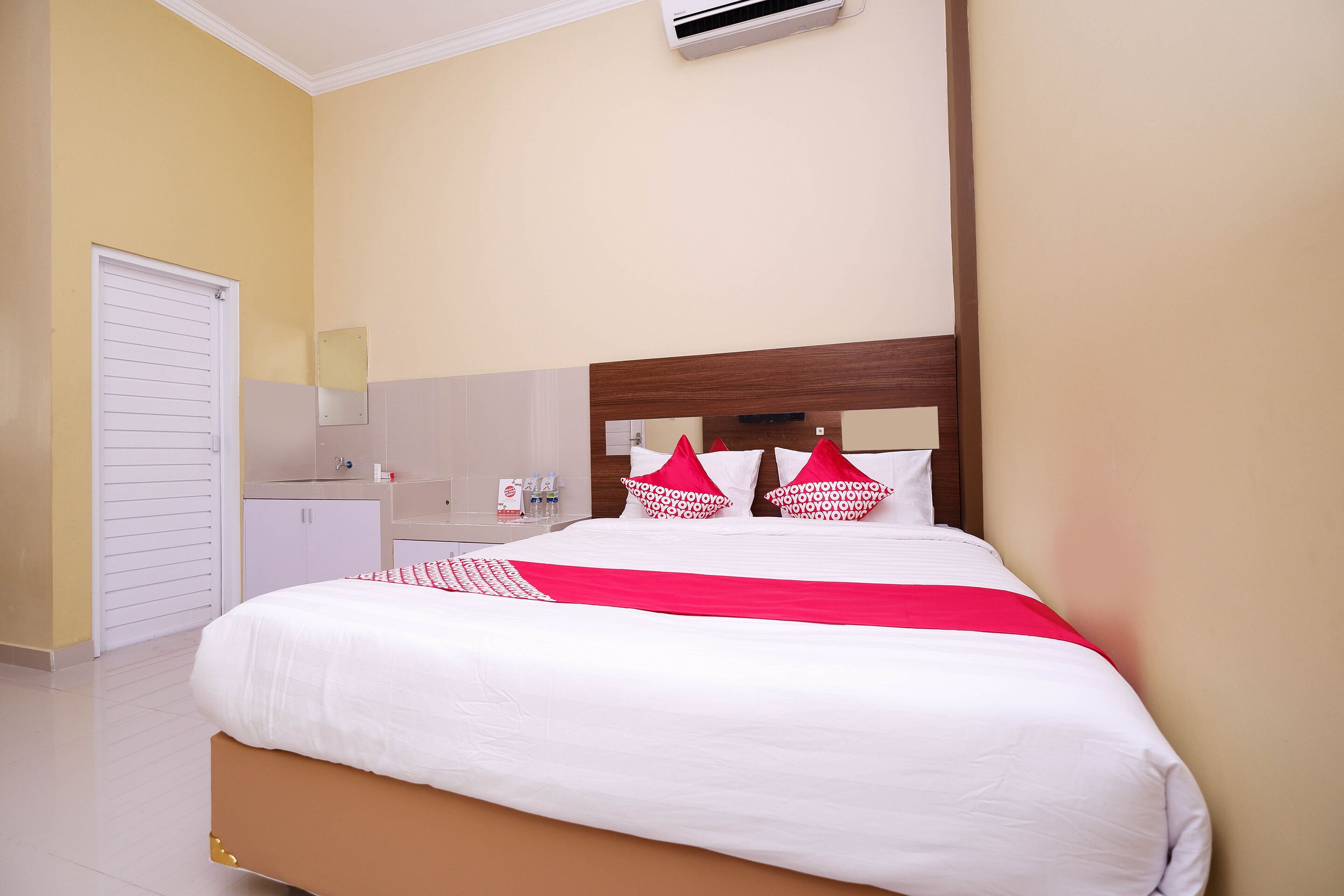 A neatly made bed with white and red bedding, a wooden headboard, and a small bedside table with toiletries.