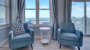 Una habitación con dos sillones azules, una mesita blanca y ventanas grandes con cortinas.