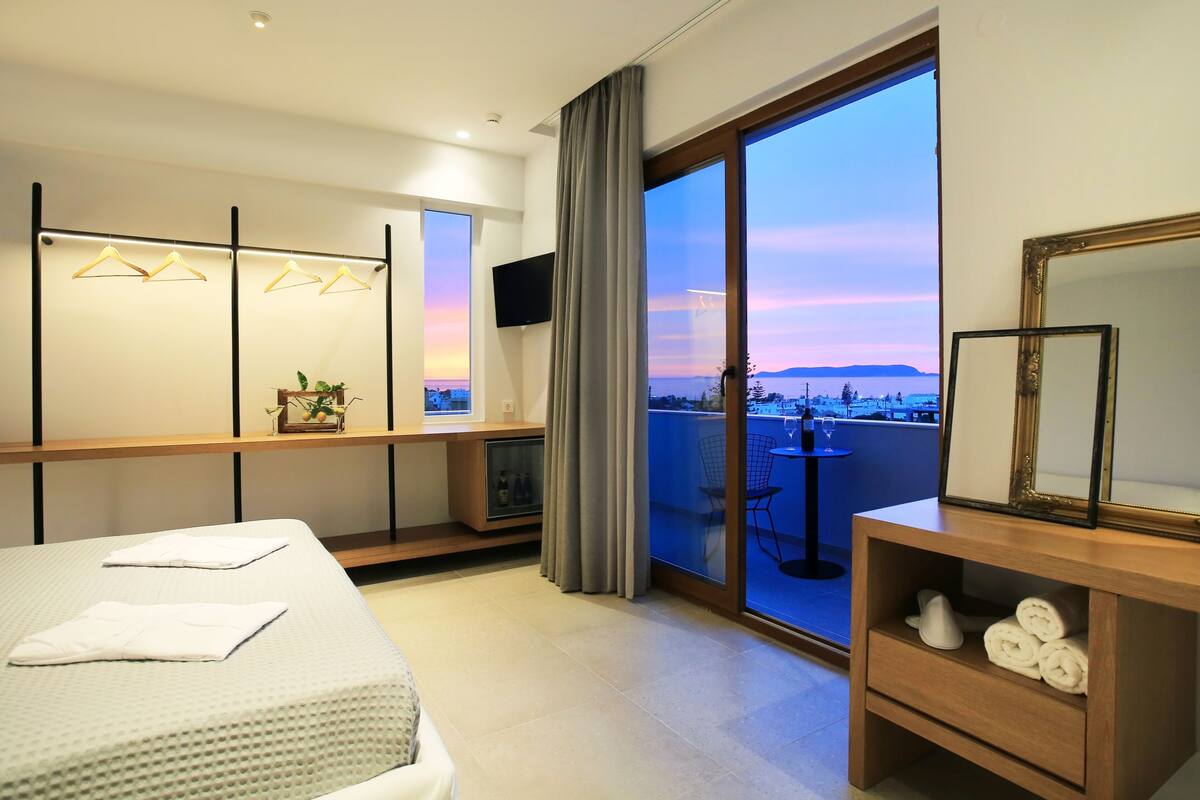 A hotel room with a bed, a TV, a balcony with a view, and a wooden nightstand with towels.