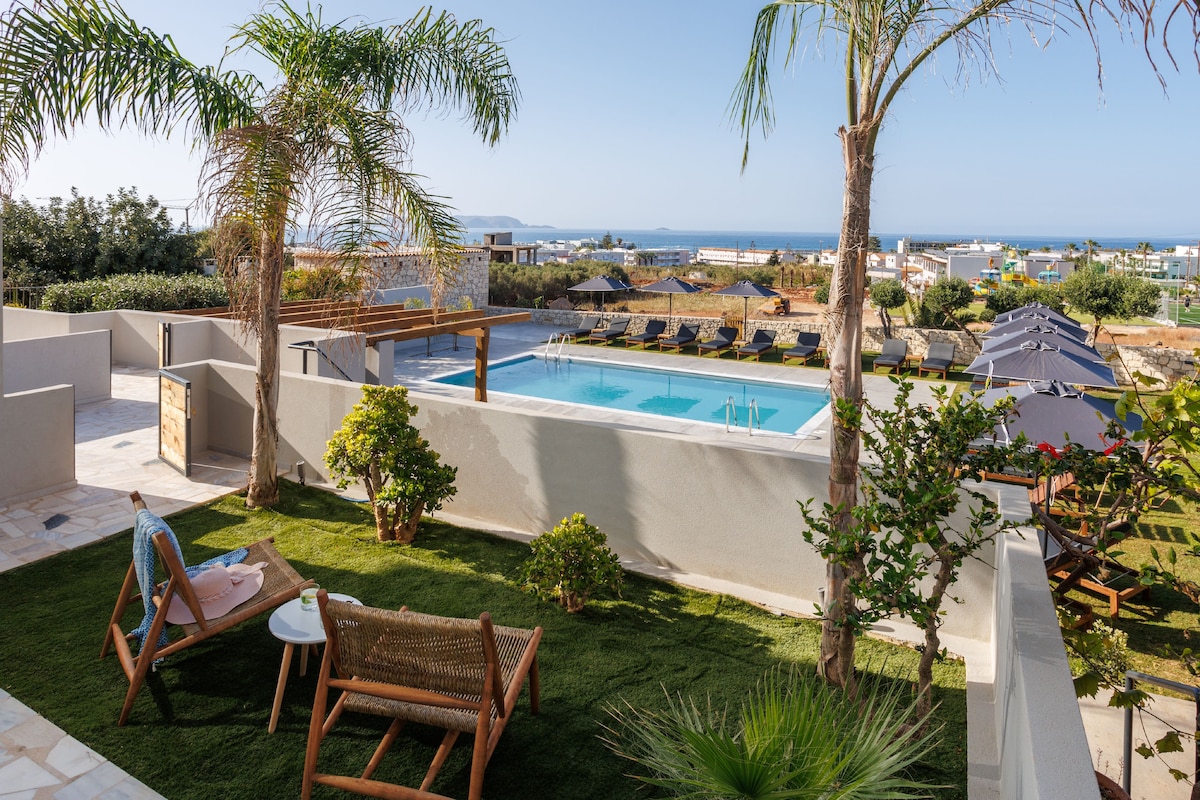 A rooftop pool with lounge chairs and a small table, surrounded by greenery and a view of the sea.