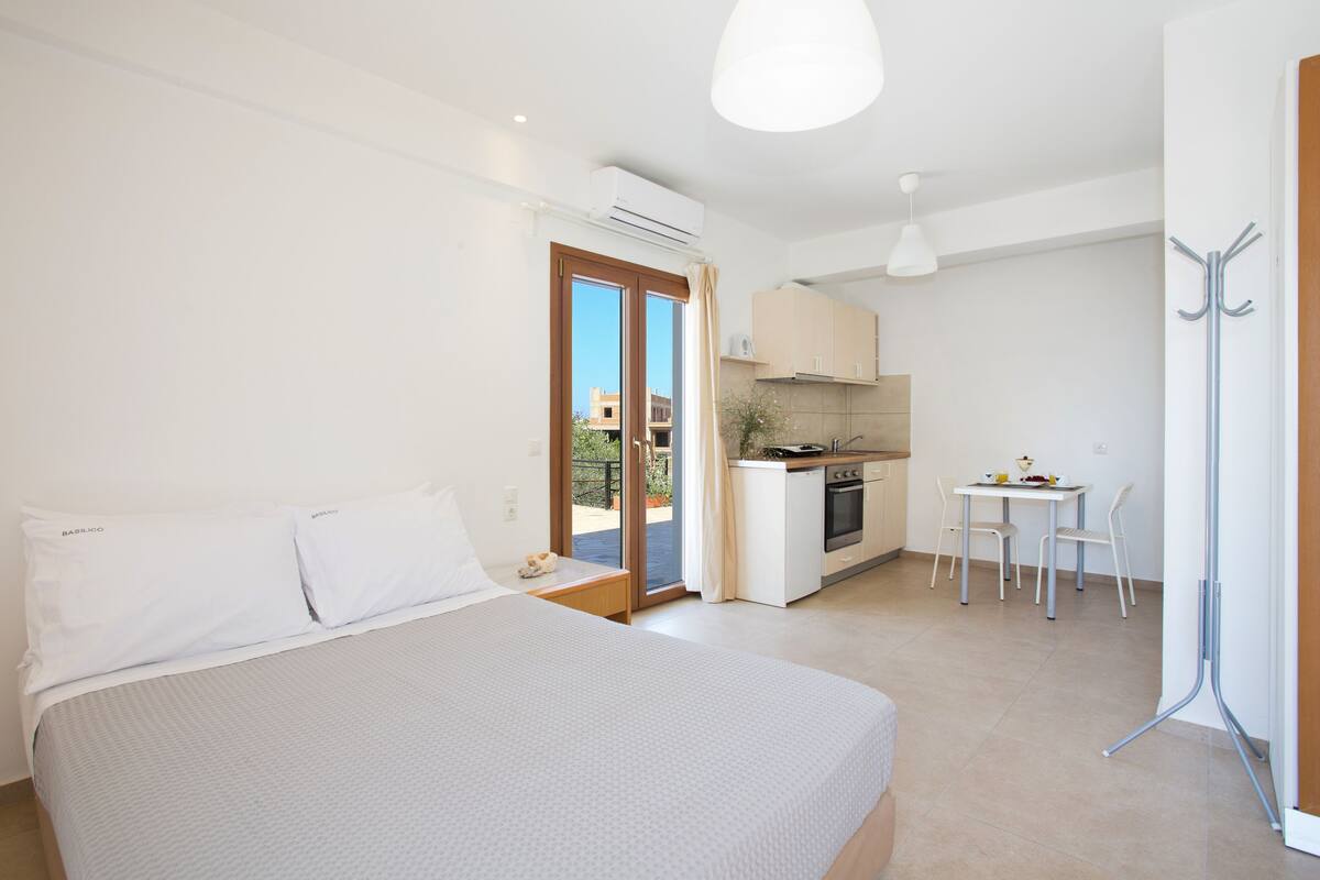 A bedroom with a large bed, a kitchenette, and a dining area.