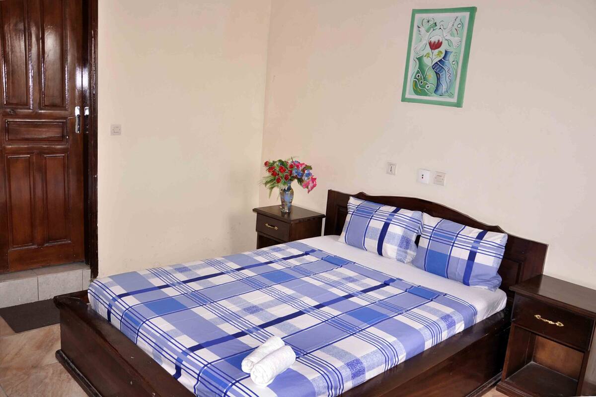 A bedroom with a wooden bed, a nightstand, a vase with flowers, and a painting on the wall.