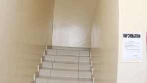 A narrow, beige-tiled staircase with a ceiling that has recessed lighting and a small circular vent. A sign on the wall to the right reads "INFORMATION." - Hotel Residence du Bonheur (Abidjan)