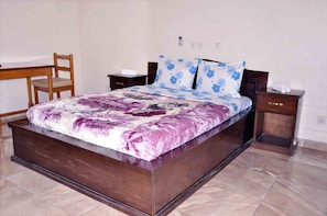 A bedroom with a large bed, a wooden chair, a nightstand, and a bedside table.