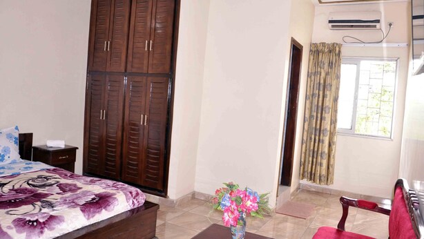 A bedroom with a bed, a wooden wardrobe, a nightstand, a chair, and a window with curtains. - Hotel Residence du Bonheur (Abidjan)