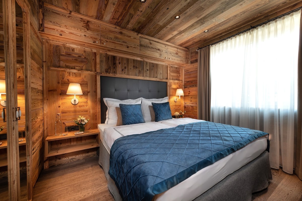 Un dormitorio con paneles de madera, una cama grande, dos mesitas de noche y una ventana con cortinas.