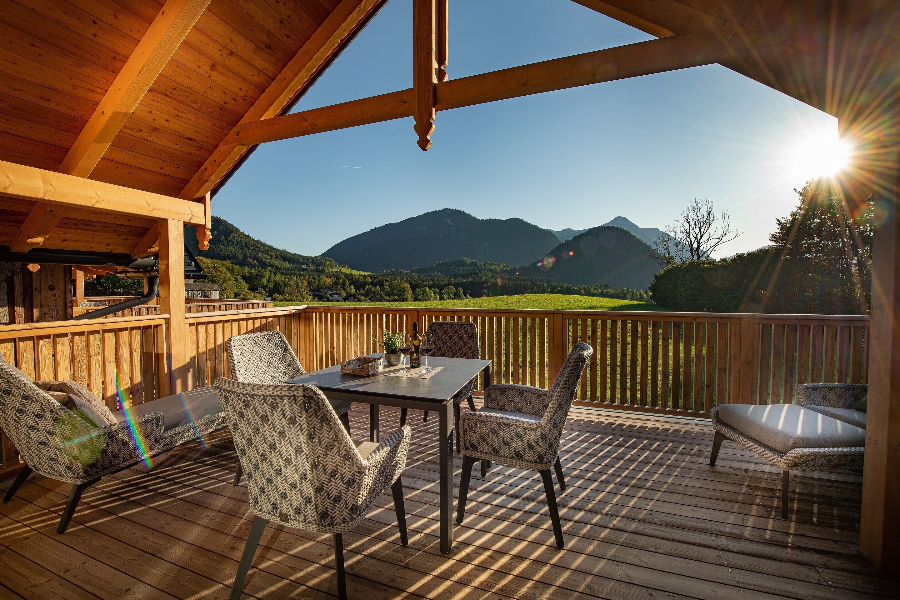 Een houten terras met een tafel en stoelen, met uitzicht op een bergachtig landschap.